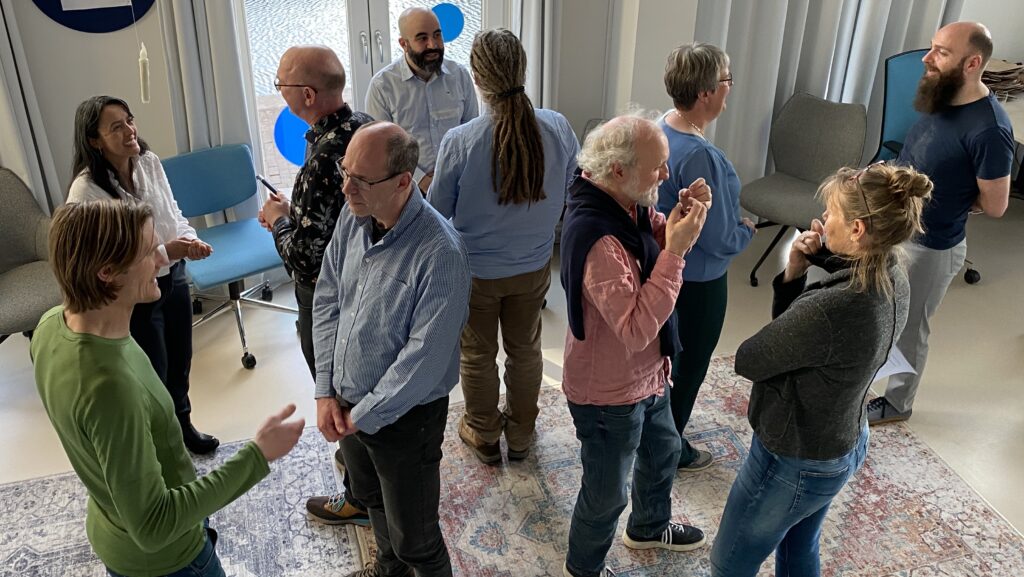 A group of about 10 standing people, that are speaking to each other in pairs.