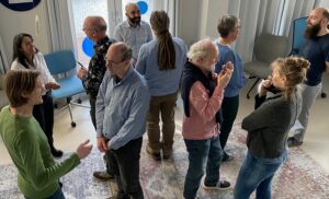 A group of about 10 standing people, that are speaking to each other in pairs.