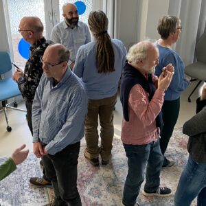 A group of about 10 standing people, that are speaking to each other in pairs.